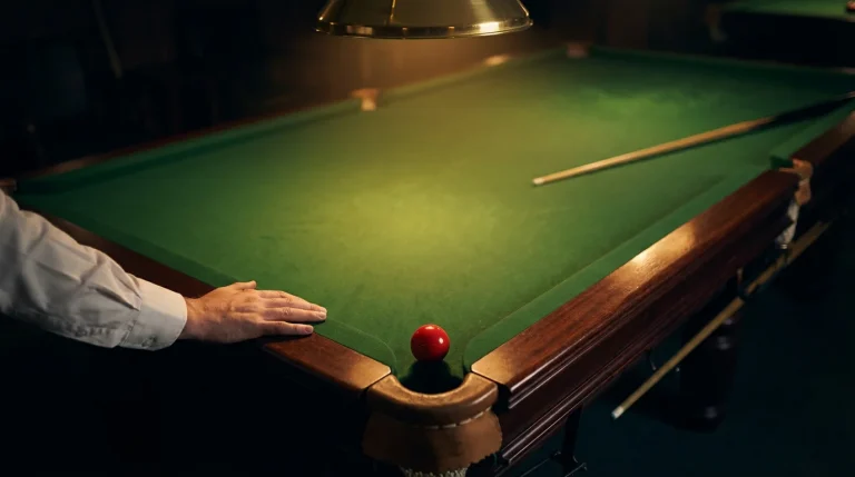 Main posée sur une table de snooker près d'une bille rouge avec un éclairage tamisé